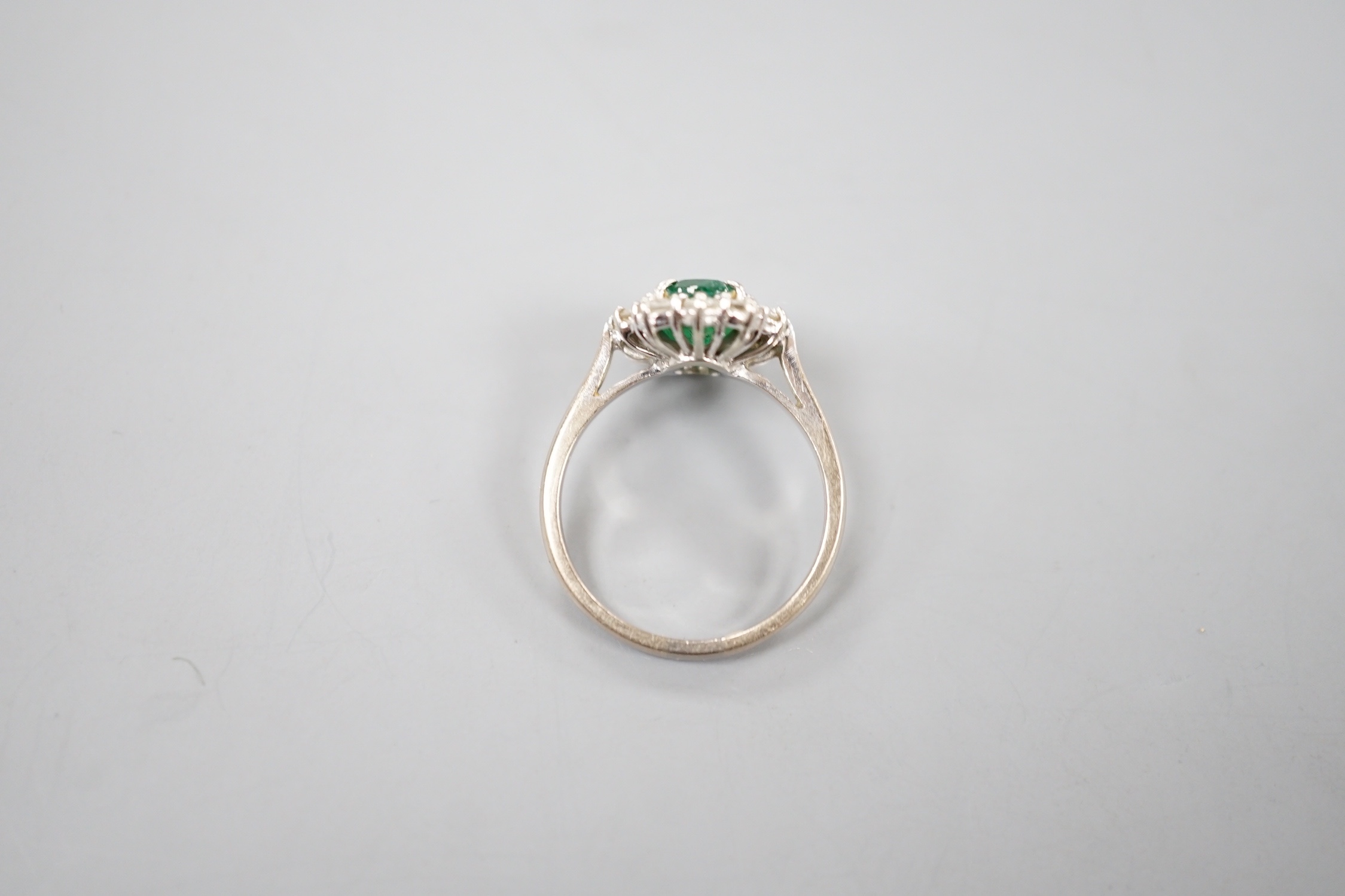 A modern 18ct white gold emerald and diamond set oval cluster ring, size O, gross weight 4.6 grams.